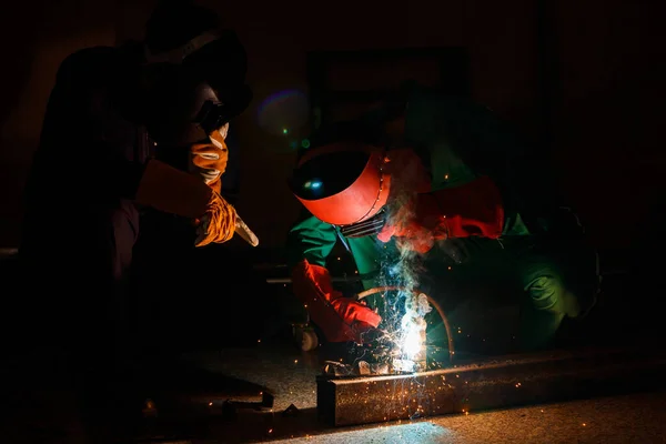 Mechanics workers work overtime hardly at night in a factory. Engineers wearing safety outfits with mechanic  jumpsuits, gloves, boots, and welding helmets working on metal welding.