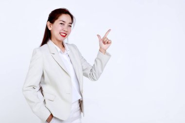 Şık takım elbiseli, kendine güvenen genç Asyalı iş kadını gülümseyip beyaz arka planda boş bir alanı işaret ediyor.