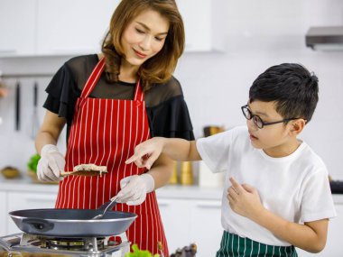 Evdeki hafif modern mutfakta bir kadınla hamburger pişirirken Asyalı çocuk Patty 'yi işaret ediyor. Çocuk konsept yaparak öğreniyor.