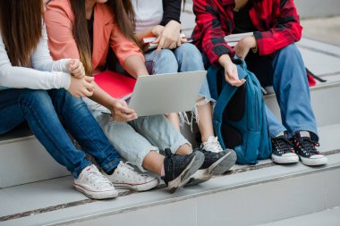 Üniversite kampüsünün açıklarında dört genç kız kolej öğrencisinin bacakları ve spor ayakkabıları yan yana oturuyor. Eğitim, arkadaşlık ve üniversite öğrencilerinin hayatı kavramı.