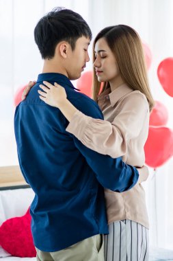 Sevgililer Günü 'nde romantik bir randevu sırasında ışık odasında gözleri kapalı dans eden Asyalı erkek ve kadının yan görüntüsü