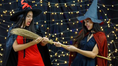 Cadılar Bayramı 'nda süpürge için mücadele eden cadı kıyafetleri ve şapkaları içindeki öfkeli genç kadınlar.