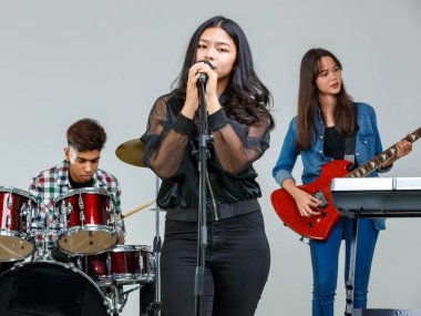 Hafta sonları müzik çalan ve birlikte şarkı söyleyen genç müzisyenlerin grup fotoğrafı. Ortaokul öğrencileri stüdyoda elektro gitar, davul ve klavye çalarken, ana vokalist önde şarkı söylüyor.