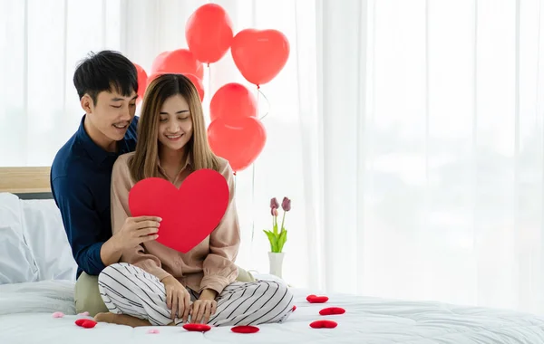 陽気なアジアの男とともに心笑顔ながら巨大ガールフレンドと休息上のベッドでバレンタインデーのお祝い — ストック写真