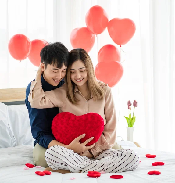 リラックスしながら ベッドの上でお互いを受け入れながら ハート型のクッション笑顔を持つ楽観的な若いアジアのカップル 十代の恋人の概念の愛と関係 — ストック写真