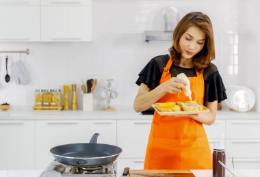 Annem turuncu önlüklü modern evde uçan tava ve gaz sobasının yanında duruyor aile kahvaltısı için kızarmış ekmek hazırlıyor.