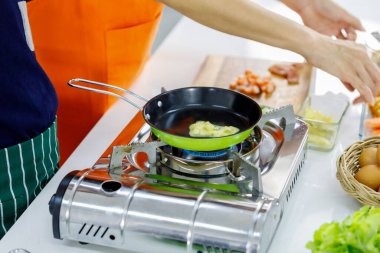 Metal gaz sobasında yeşil uçan tavada kızartılmış hammaddeden buharlaşan buhar, anne ve çocuğun evde yaptığı sağlıklı aile yemekleri için pişirmeye başlıyor.