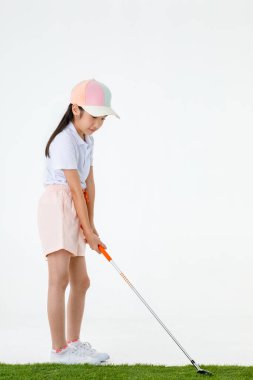 Küçük sevimli Asyalı golfçünün, spor üniformalı ve yeşil çimlerin üzerinde durup turuncu saplı beyaz arka planda golf sopası sürücüsünün portresi..