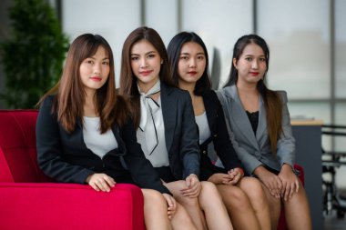Resmi takım elbiseli dört çekici Asyalı bayan ofis arkadaşı ofiste kırmızı koltukta oturmuş kameraya gülümsüyor. Modern ofis çalışması kavramı.