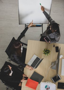 Resmi takım elbiseli Asyalı dört çekici bayan ofis arkadaşının masa başında bilgisayar masaüstü ve dizüstü bilgisayarla birlikte çalışmalarının kuş bakışı görüntüsü..