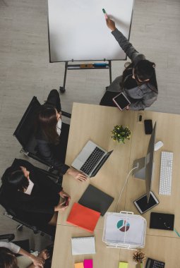 Resmi takım elbiseli Asyalı dört çekici bayan ofis arkadaşının masa başında bilgisayar masaüstü ve dizüstü bilgisayarla birlikte çalışmalarının kuş bakışı görüntüsü..