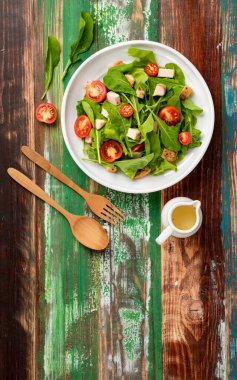Domatesli taze ıspanak salatası, beyaz seramik tabakta kızartılmış küçük sebzeli tavuk parçaları ve renkli ahşap masa üzerinde küçük bir kavanoz zeytinyağı ve ahşap çatal. Sağlıklı kavram.