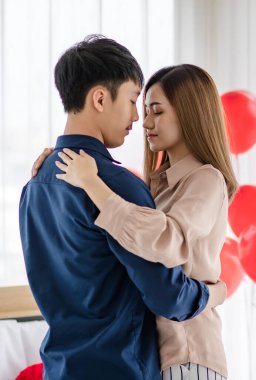 Sevgililer Günü 'nde romantik bir randevu sırasında ışık odasında gözleri kapalı dans eden Asyalı erkek ve kadının yan görüntüsü