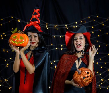 Cadı kıyafetleri içinde ve ellerinde balkabağı kafaları olan genç bayan arkadaşlar Cadılar Bayramı partisinde eğleniyorlar.