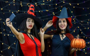 Cadılar Bayramı 'nda eğlenirken balkabağı kafalı şık genç kız arkadaşlar akıllı telefondan selfie çekiyor.