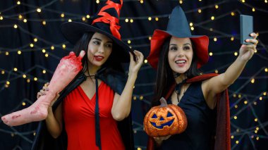 Cadılar Bayramı 'nda eğlenirken balkabağı kafalı şık genç kız arkadaşlar akıllı telefondan selfie çekiyor.