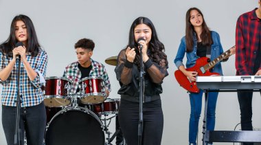 Hafta sonları müzik çalan ve birlikte şarkı söyleyen genç müzisyenlerin grup fotoğrafı. Ortaokul öğrencileri stüdyoda elektro gitar, davul ve klavye çalarken, ana vokalist önde şarkı söylüyor.