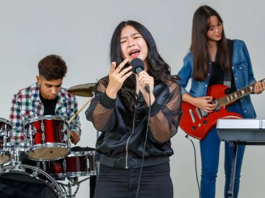 Genç şarkıcının mikrofonu tutarken ve kameraya bakarken ağzı açık bir şekilde şarkı söylediği portre çekimi. Arka planda bir müzisyenle pratik yapan mutlu öğrenci vokalist.