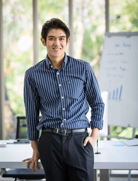 Asian handsome successful male businessman standing smiling in front of sales and marketing meeting whiteboard with graph chart data information in office room at company.