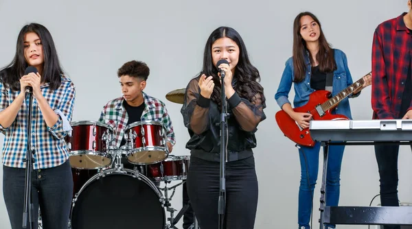 Hafta sonları müzik çalan ve birlikte şarkı söyleyen genç müzisyenlerin grup fotoğrafı. Ortaokul öğrencileri stüdyoda elektro gitar, davul ve klavye çalarken, ana vokalist önde şarkı söylüyor.