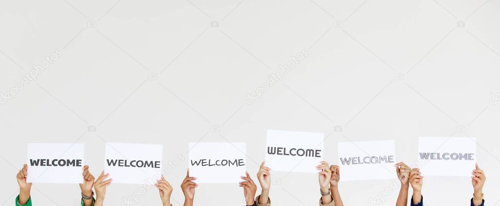 Studio shot of variety fonts welcome letters paper sign holding by unidentified unrecognizable faceless officer staff showing warm greeting to client customers or new colleagues on white background.