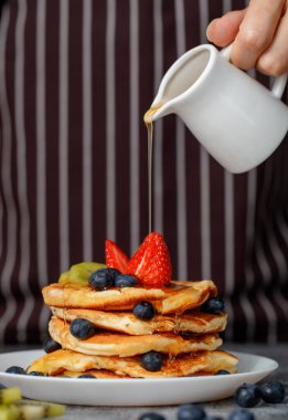 Önlüklü şef ev yapımı kreplerin üstüne beyaz seramik tabağa bal döküyor..