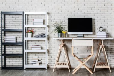 Daha az dekore edilmiş ofis konçertosu, metal raf, bilgisayar direktörü sandalyesi ve tuğla kaplamalı ahşap masa. Evde çalışma kavramı.