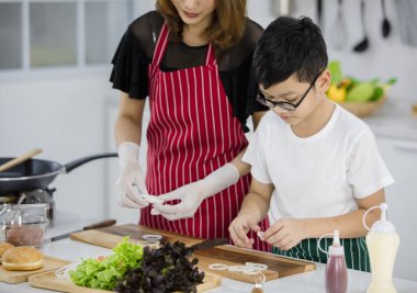 Asyalı çocuk, anne yanında taze soğan hazırlarken hafta sonu evde, modern hafif mutfakta birlikte yemek pişiriyor. Eğitim ve öğrenim kavramı.