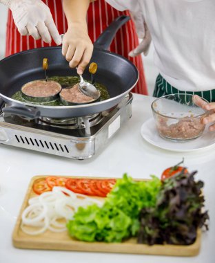 Mutfakta birlikte hamburger pişirirken önlüklü bir kadının yanında köfte yapan tanınmamış insanların yüksek açılı görüntüsü..