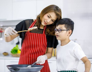 Evdeki hafif modern mutfakta bir kadınla hamburger pişirirken Asyalı çocuk Patty 'yi işaret ediyor. Çocuk konsept yaparak öğreniyor.