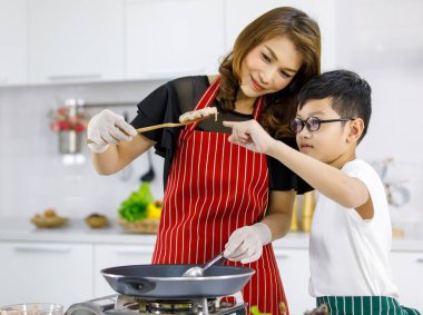 Evdeki hafif modern mutfakta bir kadınla hamburger pişirirken Asyalı çocuk Patty 'yi işaret ediyor. Çocuk konsept yaparak öğreniyor.