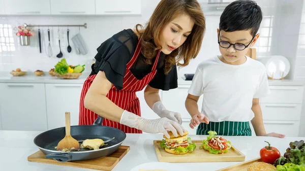 장갑입은 아시아 엄마와 주방에서 점심으로 맛있는 햄버거를 만들고 개념을 함으로써 — 스톡 사진