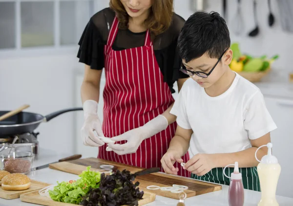 Asyalı çocuk, anne yanında taze soğan hazırlarken hafta sonu evde, modern hafif mutfakta birlikte yemek pişiriyor. Eğitim ve öğrenim kavramı.