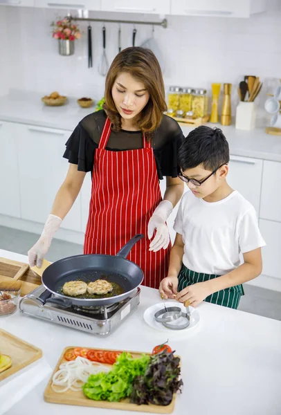 Evdeki hafif modern mutfakta bir kadınla hamburger pişirirken Asyalı çocuk Patty 'yi işaret ediyor. Çocuk konsept yaparak öğreniyor.