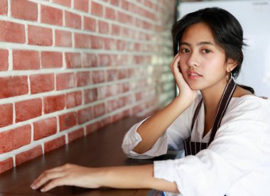 Serene Asyalı garson kafeteryada tezgahta oturuyor ve kameraya bakarken elini uzatıyor..