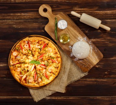 Hamur, zeytinyağı, toz ve rulo broş karides, yengeç çubuğu, çuval bezinde dolma biber ve ahşap masa ile ev yapımı deniz ürünleri pizzası yapmak için. Gıda Konsepti