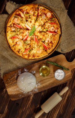 Hamur, zeytinyağı, toz ve rulo broş karides, yengeç çubuğu, çuval bezinde dolma biber ve ahşap masa ile ev yapımı deniz ürünleri pizzası yapmak için. Gıda Konsepti