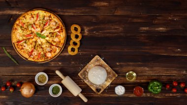 Domatesli ev yapımı deniz ürünleri pizzası, kızarmış soğan, kekik, merdane, hamurlu iğne, zeytinyağı, toz, ketçap, ahşap arka planda yer alan dolma biber tabağı.