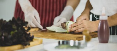 Tanınmayan bir çocuk, haftasonu evde, günümüzün hafif mutfağında birlikte yemek pişirirken kadının yanında taze soğan kesiyor. Modern çocuk eğitimi ve öğrenimi kavramı.