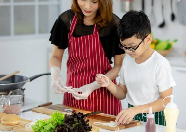 Asyalı çocuk, anne yanında taze soğan hazırlarken hafta sonu evde, modern hafif mutfakta birlikte yemek pişiriyor. Eğitim ve öğrenim kavramı.
