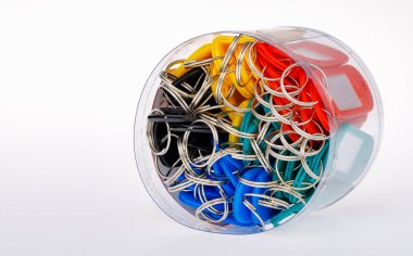 Açık, yuvarlak, plastik bir silindir kutu. İçinde kırmızı, sarı ve yeşil plastik etiketli, içinde beyaz karton kağıt bulunan metal halkalı anahtarlık var. Beyaz arkaplanda izole.