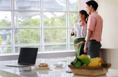 Asyalı, genç, mutlu koca ve güzel eş aşıkları gülümsüyor. Dışarıya bakıp, bilgisayar tezahüratları yapıyor ve oturma odasındaki cam pencerelerin yanında birlikte espresso içiyorlar..