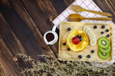 Lüks ve sağlıklı yemekler için çilek, yaban mersini, muz ve kivi karışımı lezzetli bir tatlı. Bir kavanoz tatlı şurubu, ahşap çatal ve beyaz önlük üzerine kaşık.