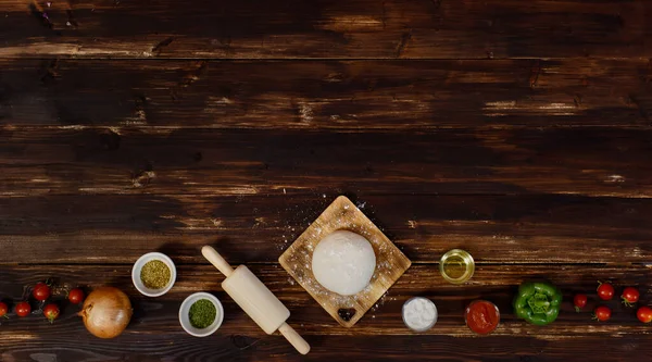 Banner of tomatoes, onion, oregano, rolling pin, dough, olive oil, powder, ketchup, bell peppers for making homemade pizza located in row form below the wooden background with copy space above