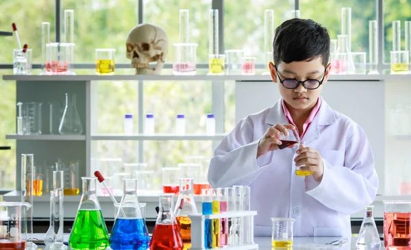 白衣を着たアジア系の子供と黄色の液体をフラスコに流し込みながら 実験室で化学研究中にカラフルな試薬で実験を行う — ストック写真