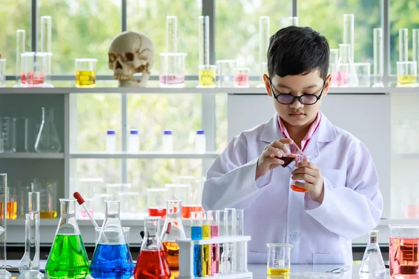 白衣を着たアジア系の子供と黄色の液体をフラスコに流し込みながら 実験室で化学研究中にカラフルな試薬で実験を行う — ストック写真