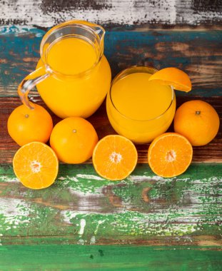 Temiz kavanozda taze portakal suyu ve renkli ahşap masada taze portakalla süsleme. Sağlıklı beslenme için stüdyo resmi konsepti. Stüdyo resmi.