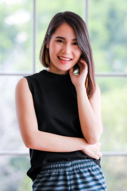 Siyahlar içinde şık düz saçlı, gülümseyen Asyalı bir kadının dikey portresi. Durup kameraya bakıyor..