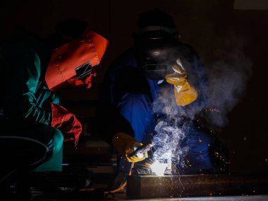 Tamirciler geceleri fabrikada fazla mesai yapmazlar. Tamirci tulumları, eldivenleri, botları ve metal kaynaklama kaskları olan güvenlik kıyafetleri giyen mühendisler..