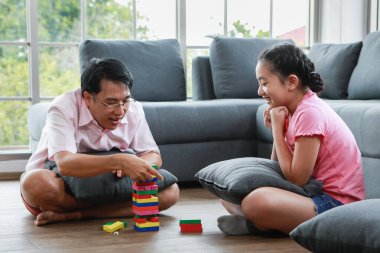 Mutlu kızı olan neşeli, genç Asyalı bir adam kanepenin yanında oturuyor ve hafta sonu evde kule oyunu oynuyor.